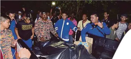  ?? PIC BY SYARAFIQ ABD SAMAD ?? Policemen and firemen placing the body of one of the drowned victims into a van in Bukit Beruntung yesterday.