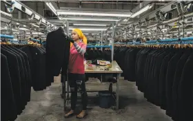  ??  ?? A worker hangs up a suit at the Man Ou Garment Co. factory in Cambodia. Companies are reconsider­ing where to put factories outside of China.