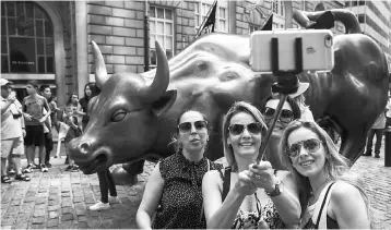  ??  ?? Tourists pose for wefie with a landmark statue of a bull in New York in this file photo. Changing technologi­es and globalisat­ion have put a premium on completing a college education in order to get and keep higher-paying jobs, Federal Reserve Chair...