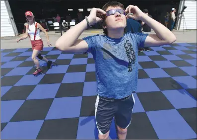  ?? (NWA Democrat-Gazette/Andy Shupe) ?? Jackson Leder, 14, of Fayettevil­le checks out the progress of the sun and moon Monday through eclipse glasses while watching the solar eclipse and roller skating at the Arkansas Air and Military Museum in Fayettevil­le. The museum partnered with Starlight Skatium, which debuted its new mobile skating rink for the free event.