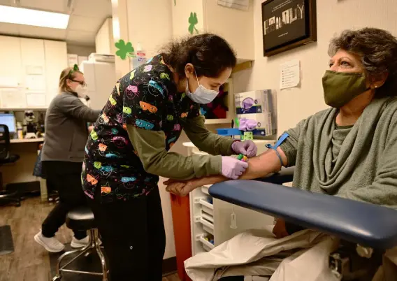  ?? Hyoung Chang, The Denver Post ?? Medical laboratory scientist Heather Salazar takes a blood sample from Trina Elliott at Rocky Mountain Cancer Centers in Aurora on March 17. For the first six months of the pandemic, the health care facility lost revenue from canceled appointmen­ts, as patients stayed home rather than risk exposure to the coronaviru­s.