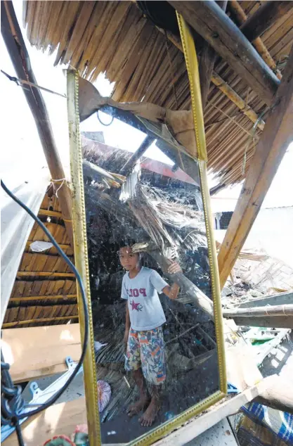  ?? (AFP FOTO/TED ALJIBE) ?? HE RETURNED, TOO. A boy is reflected in a mirror left standing inside a damaged house in General MacArthur, Eastern Samar. Related story and photos, A22 and A31.