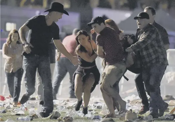  ??  ?? 0 Revellers run for cover carrying a wounded person with them after shooting broke out at the Route 91 Harvest Festival in Las Vegas