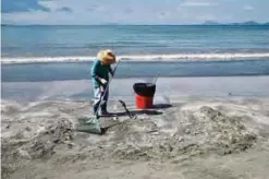  ??  ?? HONG KONG: A cleaner rakes palm oil residue from the sand on a beach in Hong Kong. —AFP