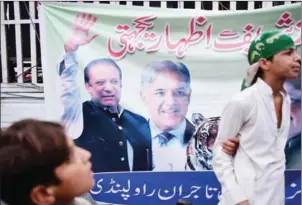  ?? AAMIR QURESHI/AFP ?? Supporters of ousted Pakistani Prime Minister Nawaz Sharif stand next to a banner featuring images of Sharif (left) and his brother Shahbaz Sharif (centre) during a rally in Rawalpindi on Saturday.