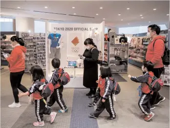  ?? AFP ?? Children walk past a Tokyo 2020 official shop in Tokyo on Wednesday, a day after the historic decision to postpone the 2020 Tokyo Olympic Games. —