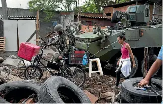  ?? PHOTO: AP ?? A Brazilian marine helps a woman with her bicycle as a barricade is removed by an armoured vehicle in Kelson’s slum in Rio de Janeiro yesterday. Members of the armed forces and police entered the slum in the first major operation since Brazil’s...