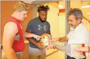  ?? Kristina Wilder / Rome City Schools ?? Players Jackson Norton (left) and JaMarcus Chatman and coach John Reid look at a pink ribbon on a Rome helmet.