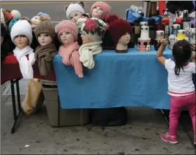  ?? AP PHOTO/JAE C. HONG ?? Mannequin heads with beanies are placed on a table as a young girl looks at goods for sale on a sidewalk on Tuesday, in Los Angeles.