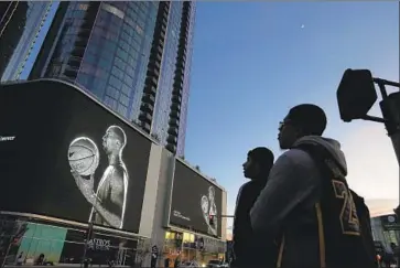  ?? Genaro Molina Los Angeles Times ?? ERIC GARCIA, left, and Ramses Dauphiney watch a memorial for Kobe Bryant in downtown L.A. on Jan. 29. Days earlier, a helicopter crash killed the Lakers star, his daughter Gianna and seven others in Calabasas.