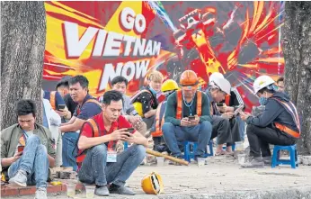  ??  ?? LEFT
Workers take a lunch break in front of a poster promoting the Vietnam Grand Prix in Hanoi.