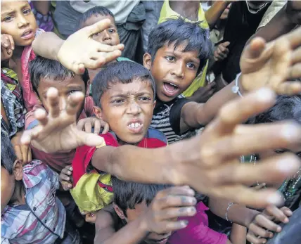  ?? Dar Yasin ?? > Rohingya Muslim children, who crossed over from Myanmar into Bangladesh, stretch out their arms out to collect chocolates and milk distribute­d by Bangladesh­i men at Taiy Khali refugee camp, Bangladesh. Inset below, Burma’s leader Aung San Suu Kyi has...