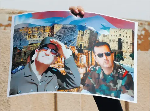  ?? LOUAI BESHARA / AFP / GETTY IMAGES ?? A Syrian protester holds a poster bearing images of the Syrian leader Bashar Assad and his late father. Removing Assad from power is now a priority for the U. S., the country’s ambassador to the United Nations said Sunday.