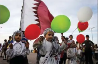  ?? HATEM MOUSSA - THE ASSOCIATED PRESS ?? In this 2012 photo, Palestinia­n children wave colored balloons and Qatari flags while waiting for the convoy of Emir of Qatar Sheikh Hamad bin Khalifa al-Thani, not pictured, to pass by a street in Gaza City.