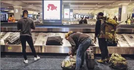  ?? Angus Mordant / Bloomberg ?? A COVID-19 advisory is displayed on a screen as travelers collect luggage in the baggage claim area of Terminal B at Laguardia Airport in New York on Monday. Airlines are set to begin layoffs Thursday.