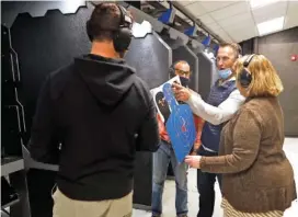  ?? AP PHOTO/SHAFKAT ANOWAR ?? Chicago resident Ray Mandel, center, shows his target to others during a shooting session at Maxon Shooter’s Supplies and Indoor Range last Friday in Des Plaines, Ill.