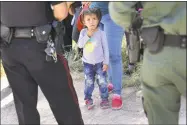  ?? John Moore / Getty Images ?? A Mission Police Department officer, left, and a U.S. Border Patrol agent watch over a group of Central American asylum seekers before taking them into custody on Tuesday near McAllen, Texas.