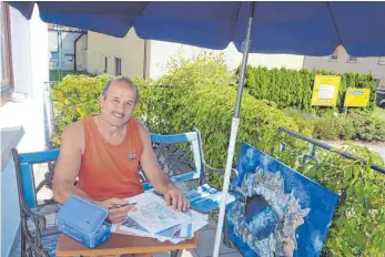  ?? FOTO: JUTTA KRIEGLER ?? Sommer auf der heimischen Terrasse: Kunstmaler Claus Schrag aus Heroldstat­t hat auch im August viel zu tun – hier mit den Skizzen für die großformat­igen Kulissenbi­lder für das Theaterstü­ck „Der Diener zweier Herren“im „Theater im Bahnof“in Rechbergha­usen bei Schwäbisch Gmünd im Ostalbkrei­s. Das blaue Bild neben ihm stammt aus seiner aktuellen Serie „Fluid Paintings.“