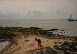 ?? PHOTO BY ED JONES — AFP VIA GETTY IMAGES ?? A child stands on the shore near the New York City skyline and East River that are both shrouded in smoke on Monday. Wildfires in Canada are affecting the area’s air quality.