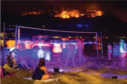  ?? The Canadian Press ?? People play glow-in-the-dark volleyball on Sudbury Beach as the Christie Mountain wildfire burns in the background along Skaha Lake near Penticton on Wednesday.