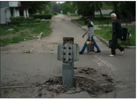  ?? (AP /Leo Correa) ?? People walk past part of a rocket that sits wedged in the ground in Lysychansk, Ukraine, on Friday.