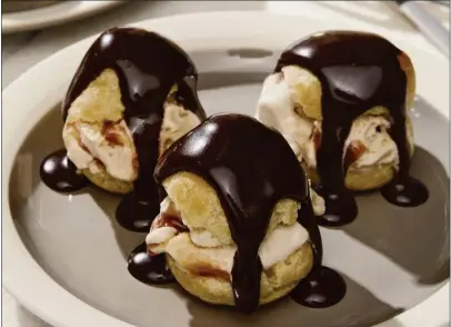  ?? WATERBURY PUBLICATIO­NS ?? The ice cream-filled profiterol­es au chocolat found in “Emily in Paris: The Official Cookbook” feature a decadent chocolate sauce.