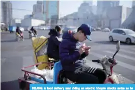  ??  ?? BEIJING: A food delivery man riding an electric tricycle checks notes as he waits to cross an intersecti­on in Beijing yesterday. —AFP