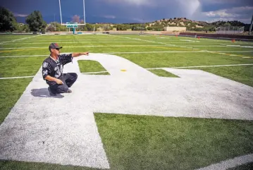  ?? GABRIELA CAMPOS/THE NEW MEXICAN ?? Aaron Gallegos, a maintenanc­e technician for Pojoaque Valley High School, crouches on the white P in the middle of the football field that had been soaked in oil and gas the previous night and points to a nearby concession stand that was also damaged.