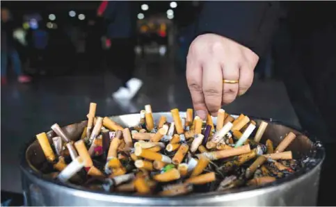  ?? —AFP ?? SHANGHAI: This file photo shows a man grinding out his cigarette in an ashtray at a railway station in Shanghai.