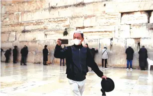  ?? (Ronen Zvulun/Reuters) ?? A VISITOR wearing a flu mask takes a selfie at the Western Wall yesterday.