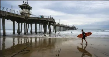  ?? ?? Under cloudy skies, a surfer walks along the beach just north of the Huntington Beach Pier on Saturday.