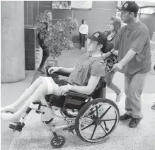  ??  ?? Humboldt Broncos hockey player Ryan Straschnit­zki, who was paralyzed following a bus crash that killed 16 people, is wheeled by his father Tom as his mother Michelle, centre, walks beside them in Calgary, Alta.