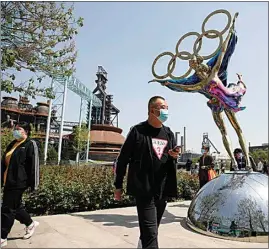  ?? ANDY WONG / AP FILE ?? Visitors wearing face masks to help curb the spread of the coronaviru­s walk by a statue featuring Winter Olympics figure skating on display at the Shougang Park in Beijing on May 2. Making an Olympic team is hard enough. This winter, those who earn their spots on the U.S. squad will find it takes even more work to get to Beijing.