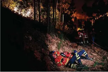  ?? Patricia del Melo / AFP / Getty Images ?? Firefighte­rs rest as an inferno rages with “great violence” near them Sunday in central Portugal.