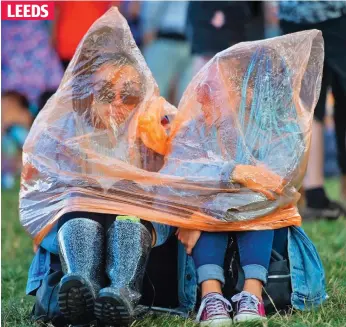  ??  ?? Damp spirits: Glum revellers huddle under a poncho yesterday