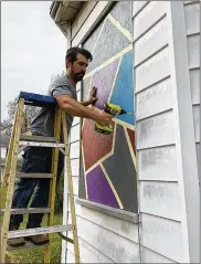  ?? PHOTO BY BRETT TURNER ?? Contractor Nate Fleming of Velorossa Design secures a window covering on an abandoned property on South Center Street. The artwork is part of a project to beautify the buildings.