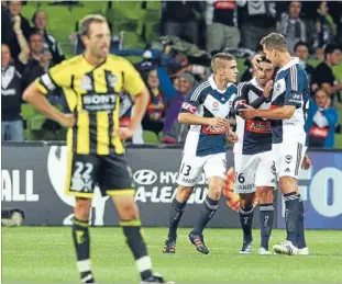  ?? Photo: GETTY IMAGES ?? Dismayed: A dejected Wellington Phoenix captain Andrew Durante looks on as Melbourne Victory’s Carlos Hernandez, centre, is congratula­ted by team-mates after he scored the opening goal in the 3-0 win on Friday night.