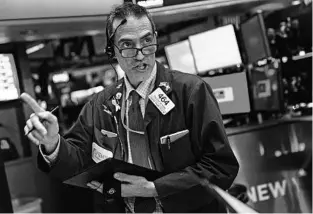  ?? JEENAH MOON/THE NEW YORK TIMES ?? A trader on the floor of the New York Stock Exchange checks the numbers as the market sell-off over the spreading coronaviru­s continued into a seventh day Friday.