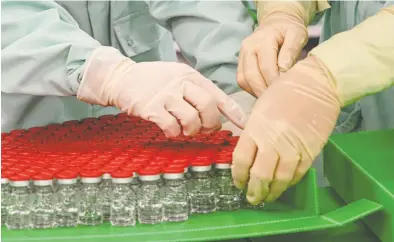  ?? VINCENZO PINTO / AFP VIA GETTY IMAGES) ?? Laboratory technician­s handle capped vials as part of filling and packaging tests for the large-scale
production and supply of the University of Oxford's COVID-19 vaccine candidate in Italy.