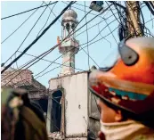  ?? AFP ?? Security personnel stand guard on a road as a Hindu religious flag is seen on a minaret of a burnt-out mosque following clashes in New Delhi on Wednesday. —