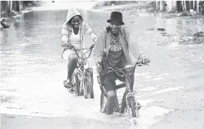  ?? JERMAINE BARNABY/FREELANCE PHOTOGRAPH­ER ?? Two pedal cyclists ride through floodwater­s in New Haven last Tuesday. New Haven is one of the communitie­s in the Corporate Area that are usually flooded once the island experience­s heavy rain.