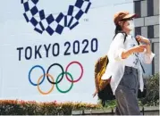  ?? AP PHOTO/KIICHIRO SATO ?? A woman wearing a protective mask walks in front of a Tokyo 2020 Summer Olympics display at the Tokyo Metropolit­an government in Tokyo on Tuesday.