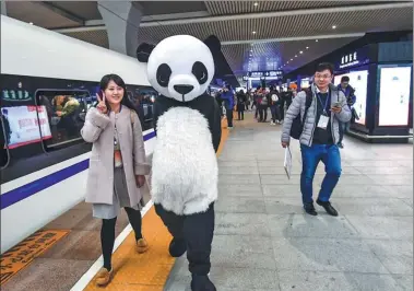  ?? LYU JIA / FOR CHINA DAILY ?? A passenger poses for a photo with a performer in a panda costume at Chengdu East Railway Station in Sichuan province on Wednesday. The Xi’an-Chengdu high-speed railway opened on Wednesday.