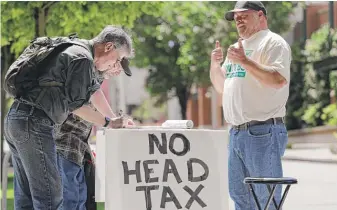  ?? ELAINETHOM­PSON/ AP ?? Paid signature gatherer John Ellard ( right) gives thumbs- up on May 24 as two men stop to sign petitions to put on the November ballot a referendum on Seattle's “head tax.”