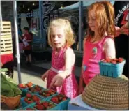  ??  ?? Fiona Ross, 6, and her older sister Julia Ross, 8, look at some fresh strawberri­es during an outdoor farmers market in Pottstown. Strawberri­es are at the top of the Dirty Dozen list which includes produce with the highest loads of pesticide residues.