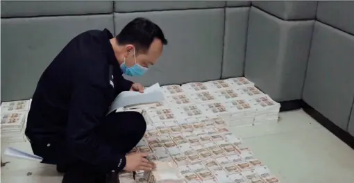  ??  ?? A police officer in Dao County inspects seized fake bank notes