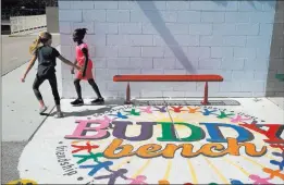  ??  ?? Third-graders Mila Lederer, left, and Chloe Anakwa walk by a buddy bench on the Walter Bracken STEAM Academy playground. This year’s Day of Caring projects will include creating a rainbow of students’ and volunteers’ handprints on the wall.