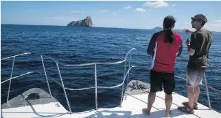  ??  ?? Guide Jorge Chavez talks with a tourist on a dive trip to Kicker Rock, visible in the distance. The towering rock formation is off the coast of San Cristobal, one of the Galapagos Islands.