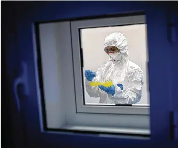  ?? OLIVER BUNIC / BLOOMBERG ?? A lab tech in biohazard coveralls does coronaviru­s tests Wednesday in an isolation chamber at a laboratory in the Torlak Institute of Virology in Belgrade, Serbia.