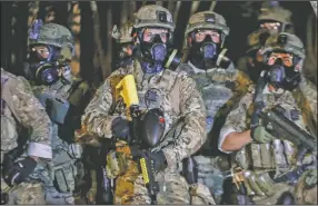  ?? (AP/The Oregonian/Beth Nakamura) ?? Law enforcemen­t officers stand ready Thursday night as protesters gather at a demonstrat­ion in Portland, Ore. Federal officers deployed tear gas and fired less-lethal rounds into a crowd of protesters late Thursday.